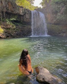 a woman sitting in the water next to a waterfall