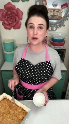 a woman wearing an apron and holding a spoon in front of a pan of food