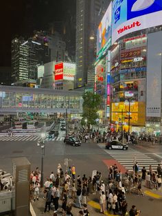 many people are crossing the street in front of some tall buildings at night with bright lights