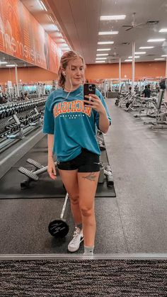 a woman taking a selfie in the gym with her cell phone and weight scale