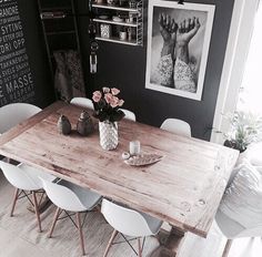 a wooden table surrounded by white chairs in a room with black walls and pictures on the wall