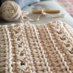 a crocheted blanket sitting on top of a couch next to a ball of yarn