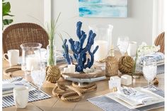 a dining room table is set with blue and white dishes, napkins, vases and candles