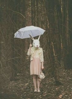 a woman holding an umbrella in the woods with a bunny mask on her head and wearing a pink dress