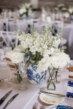 white flowers in blue and white vases on a table with silverware, plates and utensils