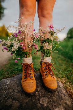 a pair of boots with flowers tied to them are standing on a rock in the grass