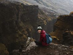 a person sitting on top of a mountain with a backpack and looking at the camera