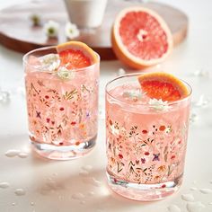 two glasses filled with blood oranges and garnished with flowers on the rim