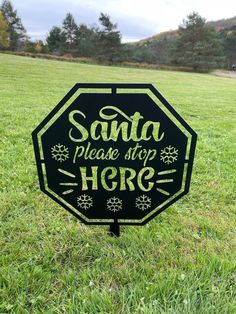 a black and white sign that says santa please stop here on it in the grass