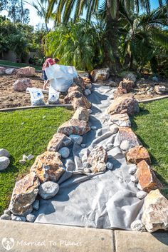 an outdoor walkway is being constructed with rocks and grass in front of a palm tree