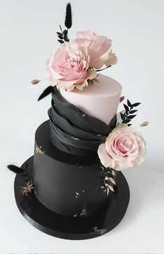 a three tiered cake with pink and black frosting, flowers and feathers on top