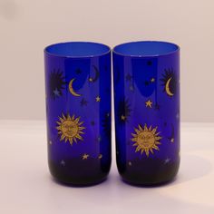 two blue glass cups with sun and moon designs on the outside, sitting side by side