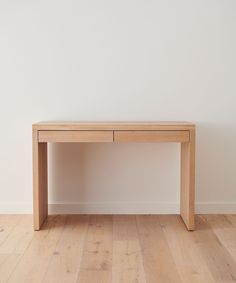 a wooden table sitting on top of a hard wood floor next to a white wall