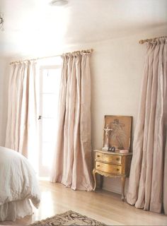 a bed sitting in a bedroom next to a window with drapes on it's sides