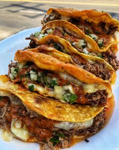 three tacos stacked on top of each other on a plate with cheese and meat