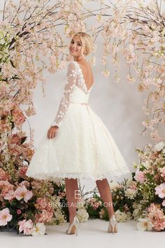 a woman standing in front of flowers wearing a white dress