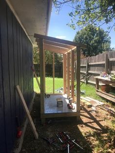 a small wooden structure sitting in the grass next to a building with tools on it