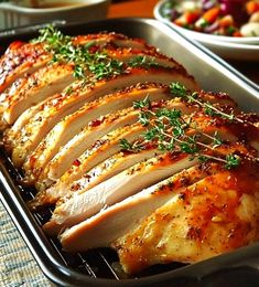 sliced chicken with herbs and seasoning in a pan on a table next to other dishes