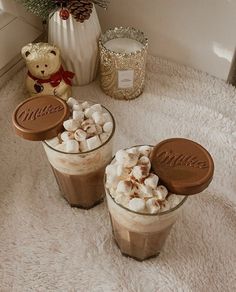 two cups filled with hot chocolate and marshmallows on top of a white rug