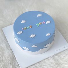 a blue cake with clouds and the words love you on it sitting on top of a white plate