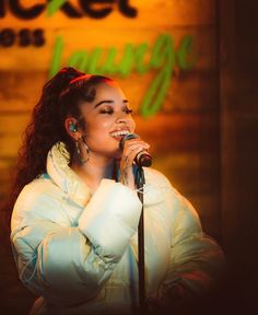 a woman singing into a microphone in front of a sign