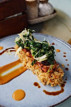 a white plate topped with rice covered in greens and sauce on top of a wooden table