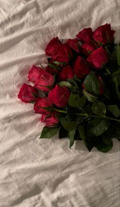 a bunch of red roses laying on top of a white sheet