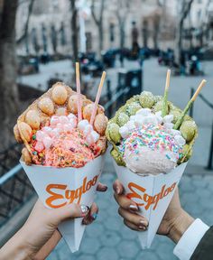 two people holding up ice cream cones filled with sprinkles and toppings