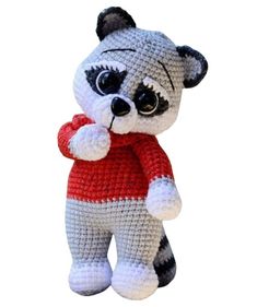 a crocheted raccoon is wearing a red shirt and holding a heart