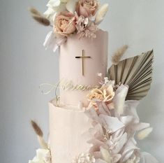 a three tiered cake with flowers and feathers on the top, decorated with a cross