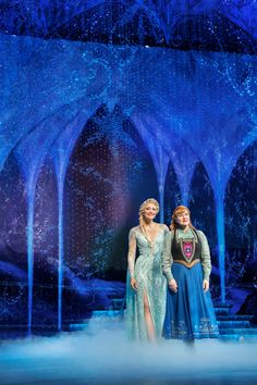 two women standing in front of a stage with snow on the ground and blue lights