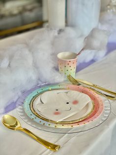 a white table topped with plates and gold utensils next to a cloud of cotton