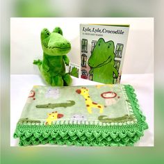 a stuffed animal next to a blanket and book on a white tablecloth with green crocheted edges