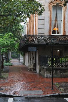 an empty street in front of a building with a lamp on the balcony and trees