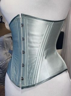 Tosca underbust corset, made in double layered silk satin. This corset is meant to be worn to emphasise the classic hourglass silhouette. Offers up to 10 cm waist reduction.  The undercup shape and hip can be shaped for perfect comfort and fit. Classic metal busk and plastic boning, steel boning available on request, please dm me for more informations. Currently available ready to ship: Sage green double layered silk satin with contrast binding. FULLY CLOSED 64 cm underbust 57 cm waist 78 cm hig Fitted Silk Corset With Boning, Underbust Corset Dress With Boning And Fitted Bodice, Satin Underbust Corset Dress With Corset Back, Fitted Silk Strapless Corset, Strapless Silk Fitted Corset, Overbust Corset With Boning And Fitted Bodice, Fitted Overbust Corset With Boning, Elegant Corset With Medium Bust Support, Elegant Corset With Medium Bust Support And Fitted Bodice