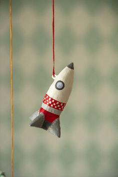 an ornament shaped like a rocket ship hanging from a string on a wall