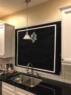 a kitchen with black counter tops and white cupboards under a hanging monogrammed sign