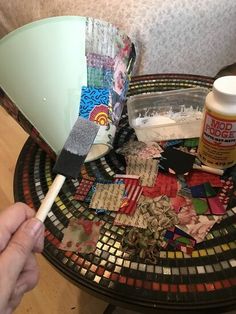 a person is holding a paintbrush over some scraps on a table with other items