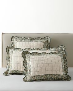 two pillows on a bed with white sheets and green trimmings, one has a decorative border around the edges