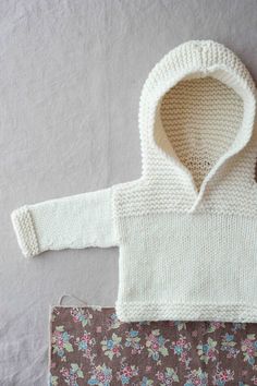 a knitted baby sweater with hood and flowered pants next to a crochet purse