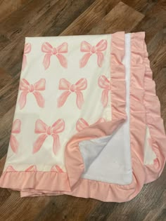 a blanket with pink bows on it laying on top of a wooden floor next to a pillow