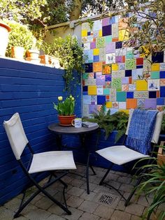 two chairs and a table in front of a blue wall with colorful tiles on it