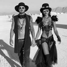 a man and woman dressed up in costumes walking on the beach with their backs to each other