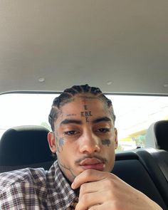 a man with tattoos on his face sitting in a car