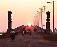 several people riding motorcycles on a bridge at sunset