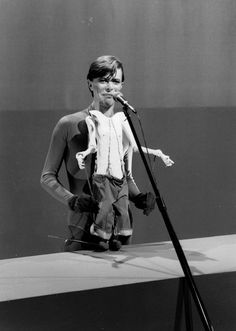 a man standing next to a microphone on top of a stage with his hands in his pockets