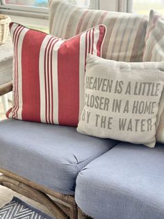 some pillows are sitting on a chair in front of a window with the words heaven is a little closer in a home by the water