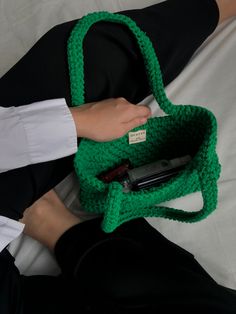 a woman is holding a green crocheted bag and cell phone in her hand