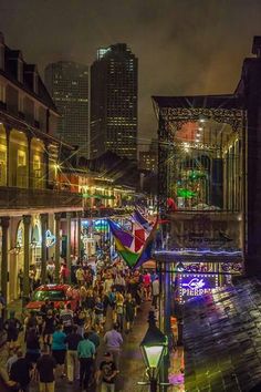 people are walking down the street at night in an urban area with tall buildings and colorful lights