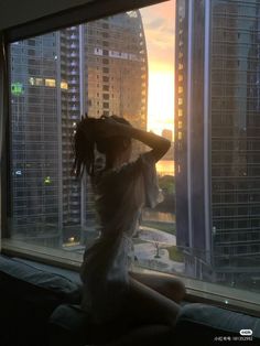 a woman sitting on top of a window sill looking out at the city skyline